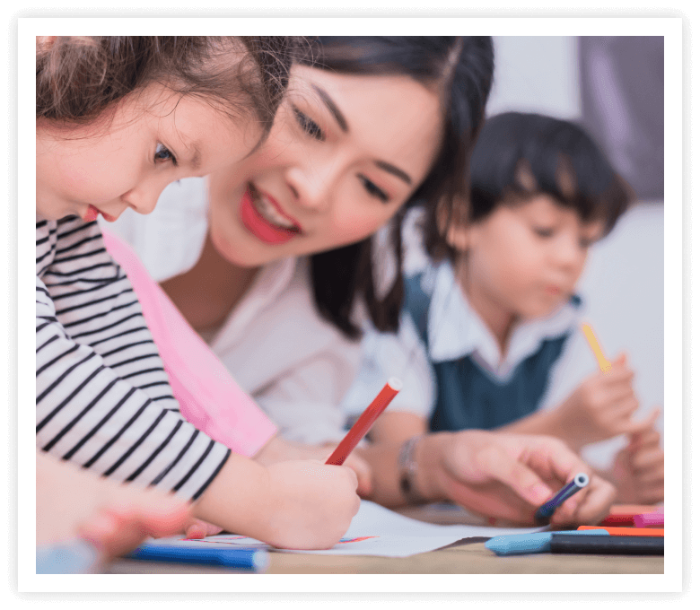 A teacher guides young children in drawing with colored pencils. The scene is warm and inviting, with a focus on creativity and learning.