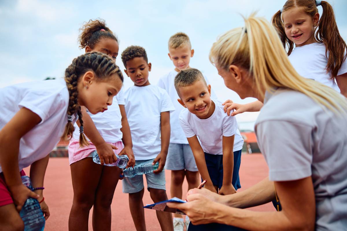 Multiracial group of children and their sports teacher talking about exercise plan at athletics club.