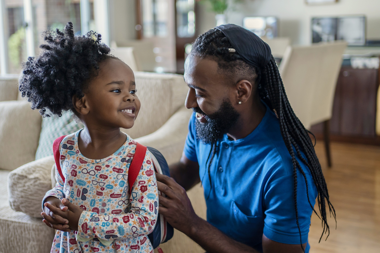 Father helping daughter to put lunch box at home